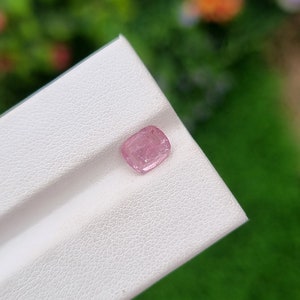 May include: A small, pink, faceted gemstone on a white background.