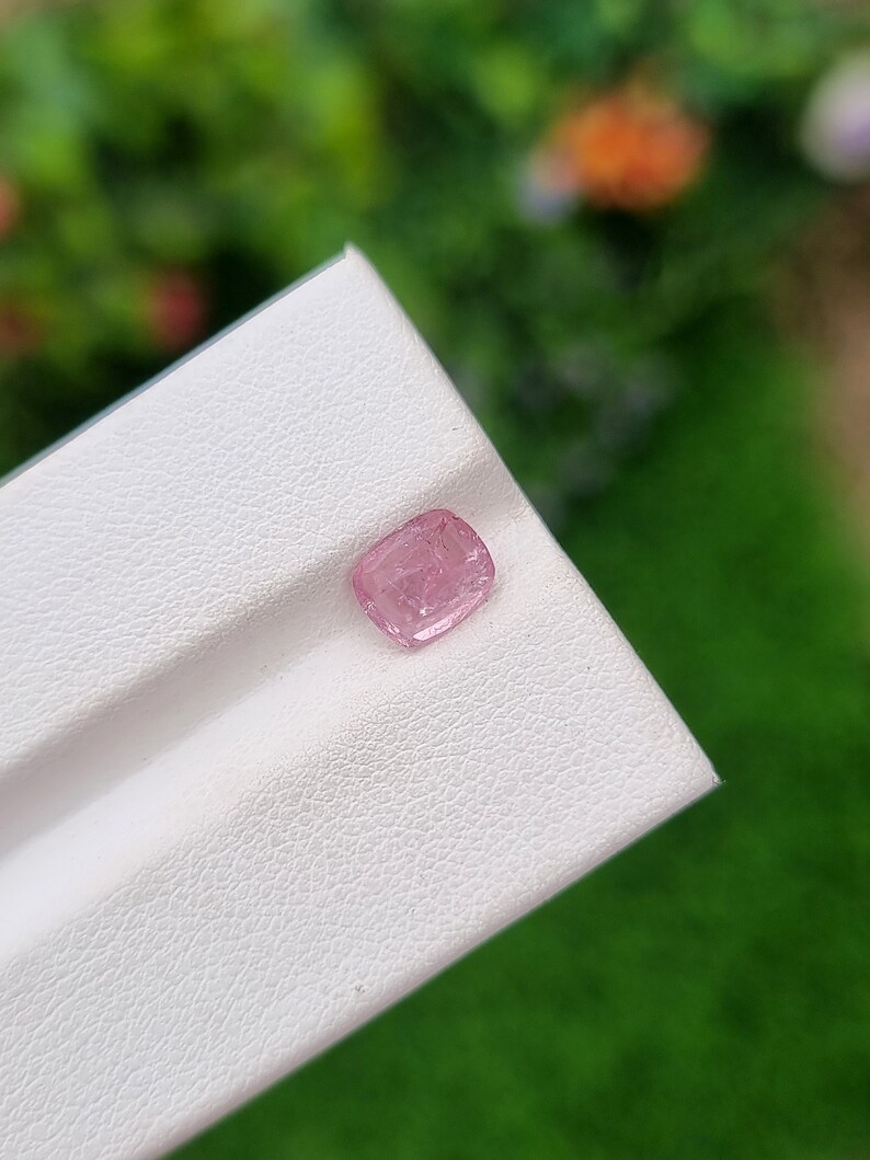 May include: A small, pink, faceted gemstone on a white background.