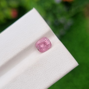 May include: A pink gemstone with a faceted cut, displayed on a white surface.
