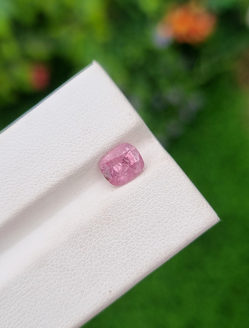 May include: A pink gemstone with a faceted cut, displayed on a white surface.