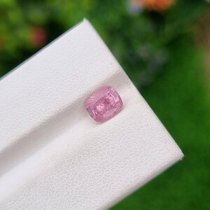 May include: A pink gemstone with a faceted cut, displayed on a white surface.