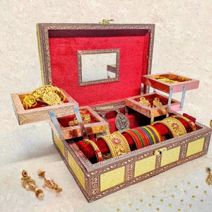 May include: A wooden jewelry box with a red velvet interior and multiple compartments. The box is open and filled with gold jewelry, including bangles, earrings, and necklaces. The box has a mirror on the inside of the lid.