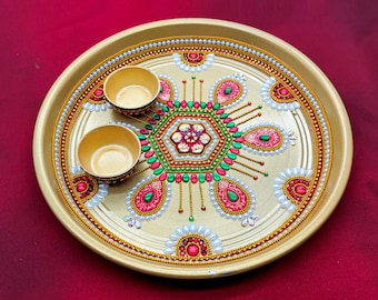 May include: A gold-colored metal plate with a decorative design featuring red, green, and white beads. Two small gold-colored bowls are placed on the plate.