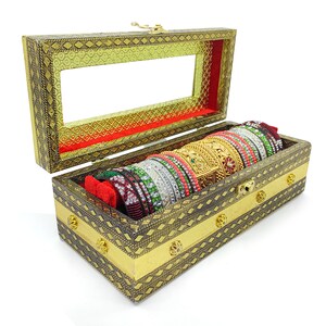 Pode incluir: Uma caixa de madeira com tampa de vidro e detalhes dourados, cheia de uma pilha de pulseiras coloridas. A caixa é decorada com padrões intrincados e tem um forro de veludo vermelho.