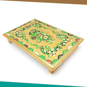 Può includere: Un vassoio in legno color oro con un bordo rialzato e quattro gambe. Il vassoio è decorato con un motivo floreale verde, rosso e nero.