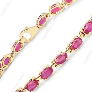 May include: A gold tennis bracelet featuring a series of oval-cut, vibrant pinkish-red rubies set in individual gold prongs. The bracelet includes a secure lobster claw clasp mechanism, creating a continuous line of gemstones and polished gold metal.