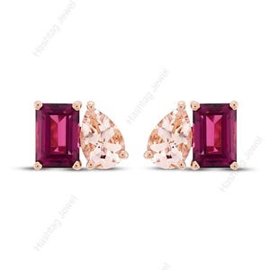 May include: A pair of stud earrings set in rose gold, each featuring a deep magenta emerald-cut gemstone paired with a pale peach pear-cut gemstone. The stones are held in place by four-prong settings, creating a symmetrical and elegant design.
