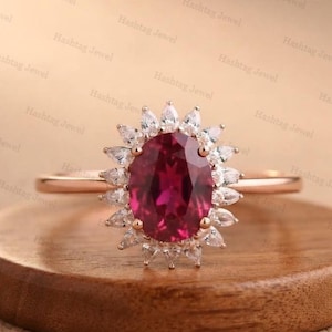 Op de afbeelding: Een roségouden ring met een grote, ovaal geslepen dieproze edelsteen in het midden, omringd door een halo van kleine, heldere, marquise-geslepen stenen in een zonnestraalpatroon. De ringband is dun, glad en gepolijst, passend bij de zetting.