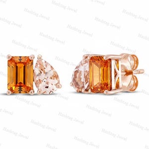 May include: A pair of stud earrings crafted in rose gold, each featuring a vibrant orange emerald-cut gemstone paired with a pale peach pear-cut gemstone. The earrings have a secure post backing and a polished metal setting that holds both stones.