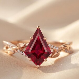 Op de afbeelding: Een roségouden ring met een dieprode edelsteen in de vorm van een vlieger, vastgehouden door zes pootjes. De ringband is ontworpen met een gedraaid rankmotief, geaccentueerd met kleine heldere steentjes langs de metalen takken.