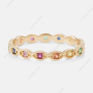 Puede incluir: Un anillo dorado con una serie de gemas coloridas. Las gemas están engastadas en un patrón repetitivo alrededor de la banda, mostrando una variedad de colores, incluyendo rosa, azul, verde y amarillo. El anillo tiene un diseño delicado y elegante.
