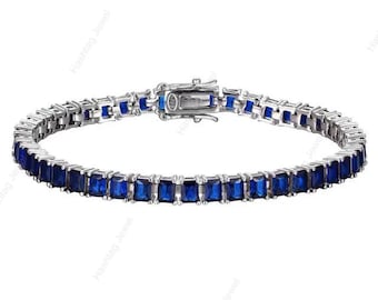 May include: A silver bracelet with a row of rectangular, deep blue gemstones. The bracelet has a secure clasp and is designed in a classic tennis bracelet style. The gemstones are evenly spaced and set in a silver metal.