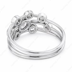 May include: A silver ring with multiple bands and bezel-set diamonds. The ring features a unique design with circular and oval diamond settings, creating a modern and elegant look. The ring is shown against a white background.