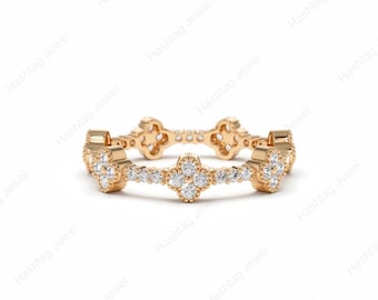 May include: A gold band ring featuring a repeating pattern of four-leaf clover motifs. Each clover is set with small, clear, round-cut stones. The band has a polished gold finish and a delicate, openwork design that encircles the entire finger.