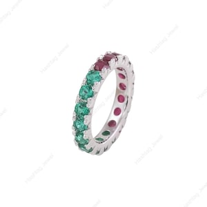 Può includere: Una fede a giro completo in argento con una fila di smeraldi verdi e rubini rosso scuro a taglio rotondo, montati con grinfie condivise. L'anello presenta un motivo continuo che alterna gemme verdi e rosse lungo tutta la fascia in metallo.