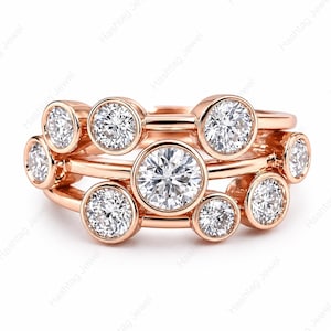 May include: Rose gold rings with multiple clear, round-cut gemstones. The rings are stacked, showcasing a variety of sizes and settings. The image is against a white background. The text "Hashtag Jewel" is visible.