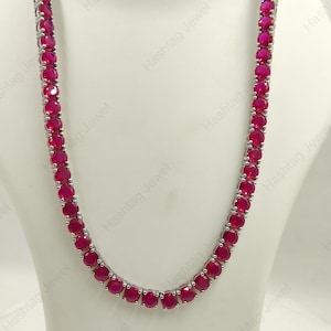 May include: A tennis necklace featuring a continuous row of round, vibrant pink stones set in a polished silver-toned metal frame. The stones are uniform in size and shape, creating a symmetrical design that drapes in a classic U-shape.