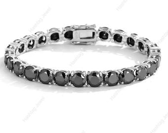 May include: A silver tennis bracelet with round, black gemstones. The bracelet features a secure clasp and is set against a white background. The gemstones are evenly spaced and reflect light.