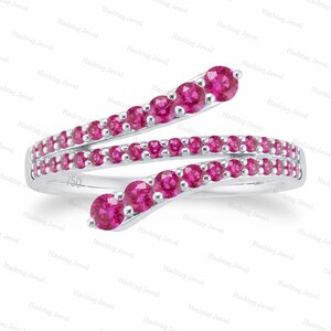 Puede incluir: Un anillo de estilo bypass hecho de metal plateado, con dos bandas superpuestas incrustadas con numerosas piedras redondas de color rosa vibrante. La banda interior tiene grabado el número 750, que indica la pureza del metal de la joya.