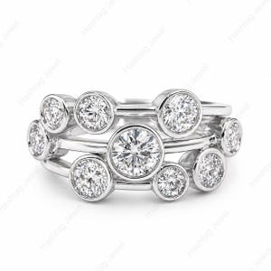 May include: A stack of three silver rings with multiple round, clear gemstones. The rings are set with bezel-set stones of varying sizes, creating a layered effect. The rings are displayed on a white background.