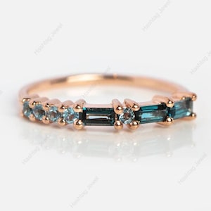 Puede incluir: Anillo de oro rosa con piedras preciosas alternas azul-verdosas en forma de baguette y redondas. La banda del anillo es de oro rosa y las piedras están engastadas en fila. Una joya para uso diario o ocasiones especiales.
