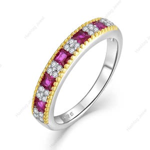 Può includere: Un anello d'argento con una fascia dorata con pietre preziose quadrate color magenta alternate e gruppi di piccole gemme bianche. L'anello è contrassegnato con "925".