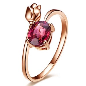 Può includere: Un anello in oro rosa con una pietra preziosa rosa e un design a forma di rosa. L'anello è un gioiello delicato.