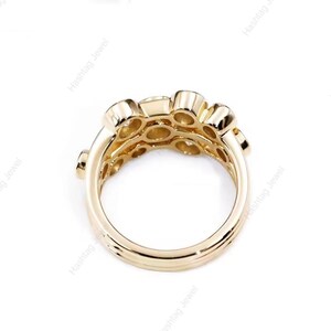 May include: A gold-colored ring with multiple round gemstones set in a cluster design. The ring has a thick band and a detailed setting, showcasing a modern and elegant style. The ring is displayed against a white background.