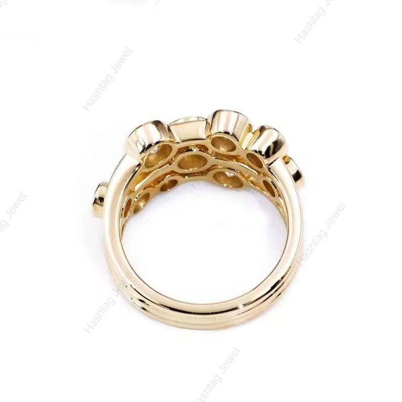 May include: A gold-colored ring with multiple round gemstones set in a cluster design. The ring has a thick band and a detailed setting, showcasing a modern and elegant style. The ring is displayed against a white background.