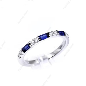 May include: A silver ring featuring alternating blue rectangular and round white gemstones. The ring is set against a white backdrop, highlighting the sparkle of the stones. A delicate piece of jewellery.