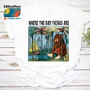 Könnte beinhalten: Weißes T-Shirt für Kleinkinder mit einer bunten Illustration eines Monsters aus dem Buch "Wo die wilden Kerle wohnen". Die Illustration zeigt das Monster, das in einem Dschungel mit einem Segelboot im Hintergrund sitzt. Der Text "Wo die bösen Dinge sind" ist über der Illustration gedruckt.