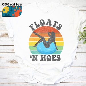 Puede incluir: Camiseta blanca con un gráfico de estilo vintage de una mujer en un flotador de piscina con el texto "FLOATS 'N HOES" en negro.