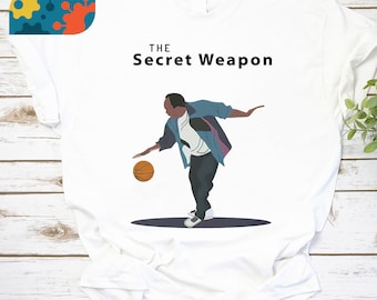 May include: White t-shirt with a graphic of a cartoon basketball player dribbling a ball. The text "THE Secret Weapon" is printed above the graphic.