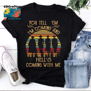 May include: Black t-shirt with a vintage-style graphic of four figures in silhouette standing in front of a sunset. The text "You tell 'em I'm coming and Hell's coming with me" is printed on the shirt.