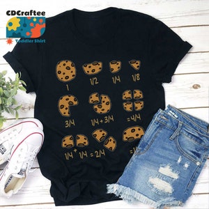 May include: A black t-shirt featuring a graphic of chocolate chip cookies divided into fractions. The graphic shows the fractions 1, 1/2, 1/4, 1/8, 3/4, 1/4 + 3/4 = 4/4, and 1/4 + 1/4 = 2/4.