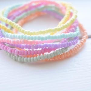 May include: A stack of pastel-colored beaded bracelets. The bracelets are made of small, round beads in shades of pink, yellow, green, and purple.