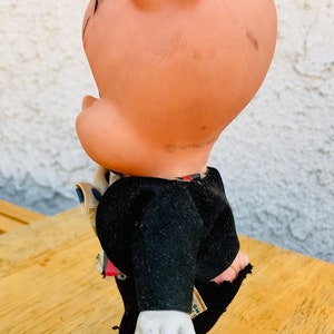 Puede incluir: Un juguete de cerdo vintage que lleva un traje negro y un sombrero rosa. El cerdo tiene una camisa blanca con una corbata de patr&oacute;n azul y blanco. El juguete est&aacute; hecho de pl&aacute;stico y tiene una cara pintada.