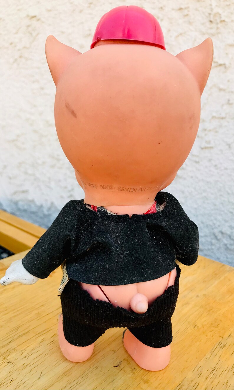 Puede incluir: Una mu&ntilde;eca de cerdo rosa con un sombrero rojo y un traje negro. La mu&ntilde;eca tiene un guante blanco en una mano y el texto "DANNER BROS. SEVEN ARTS" est&aacute; impreso en la parte posterior de la mu&ntilde;eca.