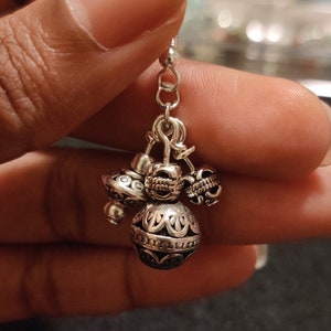 May include: Silver dangle earrings with multiple charms, including a round charm with an intricate design.