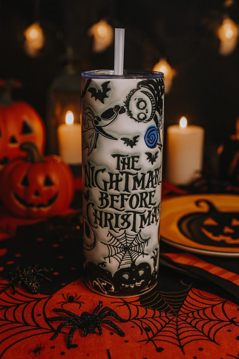 May include: A white tumbler with a straw featuring a design from "The Nightmare Before Christmas." The design includes bats, Jack Skellington, and a spiderweb. The text "The Nightmare Before Christmas" is printed on the tumbler.