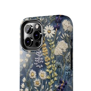 Op de afbeelding: Een blauwe telefoonhoes met een geborduurd bloemenpatroon met witte madeliefjes en groene bladeren.