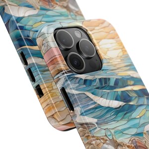 May include: A smartphone case featuring a stained glass style pattern with shades of blue, teal, white, and tan. The design depicts abstract waves and sandy textures. The case has black side buttons and a cutout for a triple camera lens system.