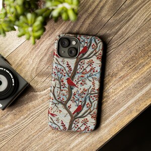May include: A phone case with a white background and a red, blue, and green floral pattern with red birds. The case has a camera lens cutout.