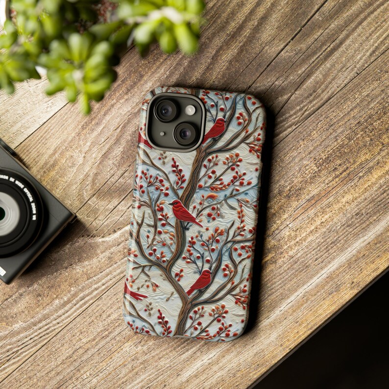 May include: A phone case with a white background and a red, blue, and green floral pattern with red birds. The case has a camera lens cutout.