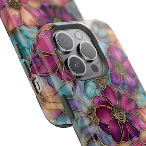 K&ouml;nnte beinhalten: Eine Smartphone-H&uuml;lle mit einem lebendigen Blumenmuster aus tief magentafarbenen, zartrosa und t&uuml;rkisblauen Bl&uuml;tenbl&auml;ttern, die mit metallischem Gold umrandet sind. Das Design umfasst einen Ausschnitt f&uuml;r die Dreifachkamera und schwarze Seitentasten.