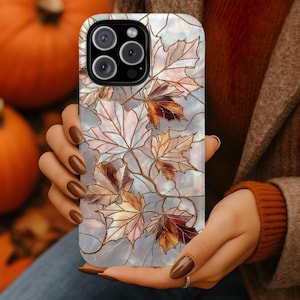 May include: A smartphone case featuring a stained glass design of autumn maple leaves in shades of brown, copper, and cream. The leaves are outlined in thin metallic lines against a pearlescent, iridescent background with a triple camera cutout.
