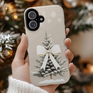 May include: A white phone case with a beige background featuring a green Christmas tree with a white bow. The tree is surrounded by white snowflakes.