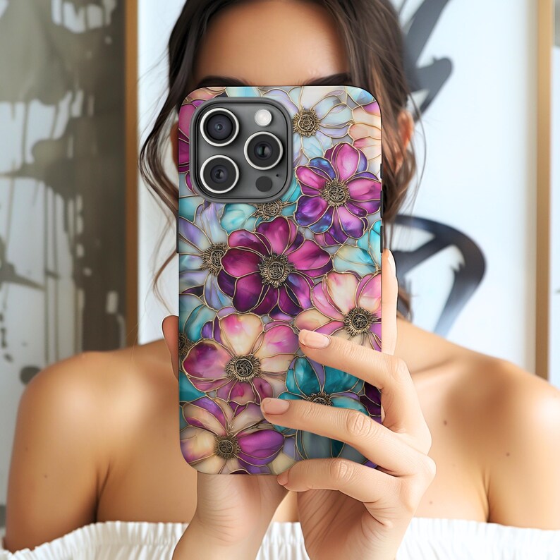 K&ouml;nnte beinhalten: Eine Smartphone-H&uuml;lle mit einem lebendigen Blumenmuster aus &uuml;berlappenden Bl&uuml;tenbl&auml;ttern in Magenta, Dunkelviolett, T&uuml;rkis und Cremewei&szlig;. Das Design weist dunkle, definierte Umrandungen um jede Bl&uuml;te auf, die einen Buntglaseffekt erzeugen.