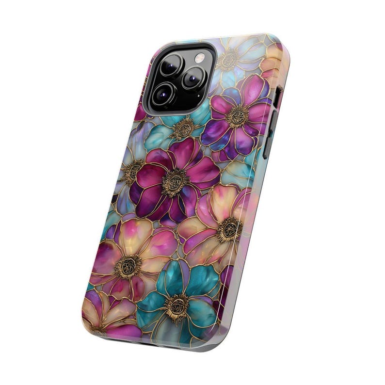 K&ouml;nnte beinhalten: Eine Smartphone-H&uuml;lle mit einem lebendigen Blumenmuster aus &uuml;berlappenden Bl&uuml;tenbl&auml;ttern in Magenta, T&uuml;rkis und hellem Gelb. Das Design zeigt goldfarbene Umrandungen um jede Blume, die einen Buntglaseffekt auf der gesamten Oberfl&auml;che erzeugen.