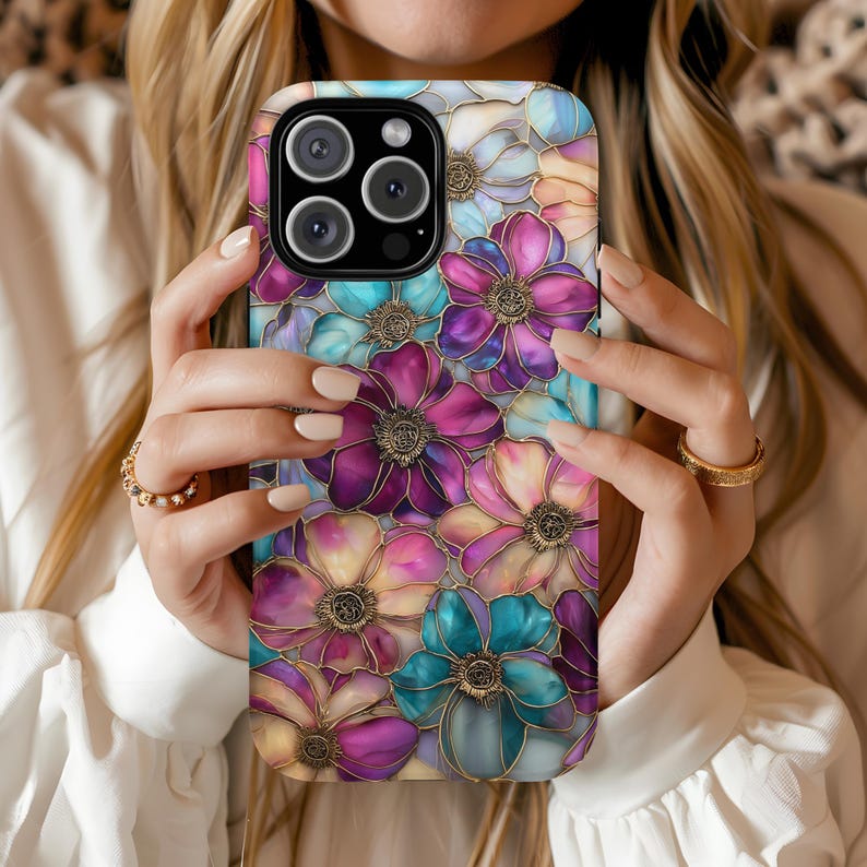 K&ouml;nnte beinhalten: Eine Smartphone-H&uuml;lle mit einem farbenfrohen Blumenmuster im Buntglas-Stil, das &uuml;berlappende Bl&uuml;tenbl&auml;tter in Magenta, T&uuml;rkis und zartem Pfirsich zeigt. Dunkle Umrandungen um jede Bl&uuml;te erzeugen eine segmentierte Optik wie bei einem Mosaik.